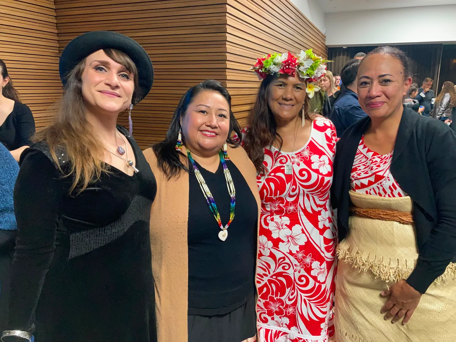 Four women standing together in front of a wood-slatted wall at an indoor event
