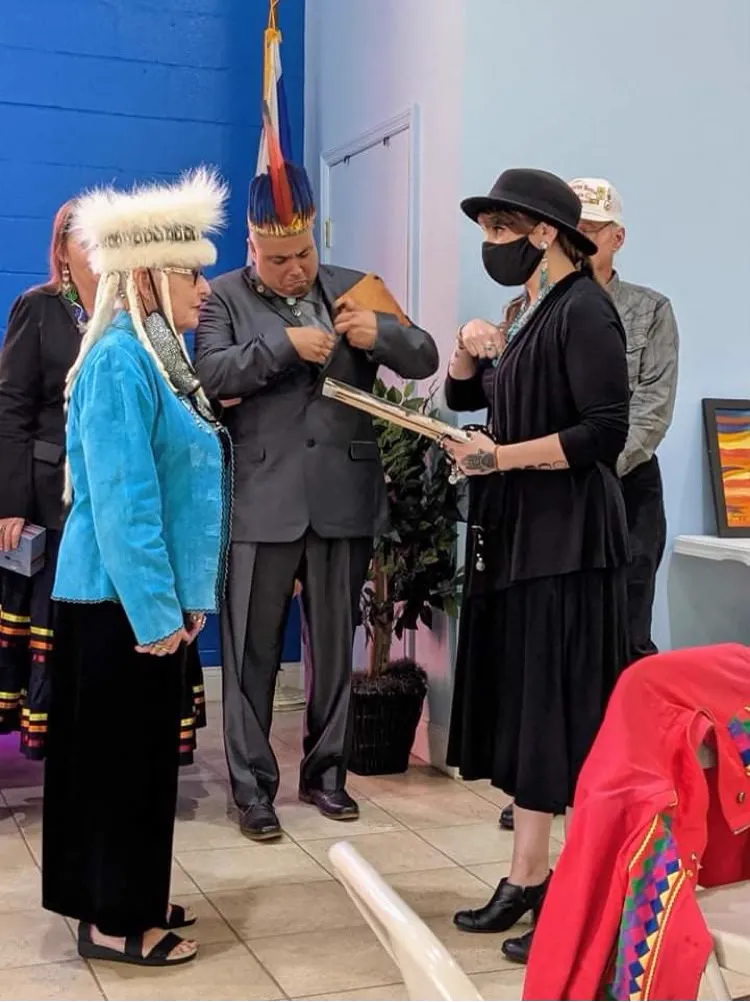 Several people in regalia and formal wear exchanging an item indoors