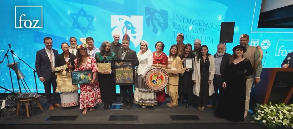 A large group on a stage holding framed artwork and gifts before a blue backdrop