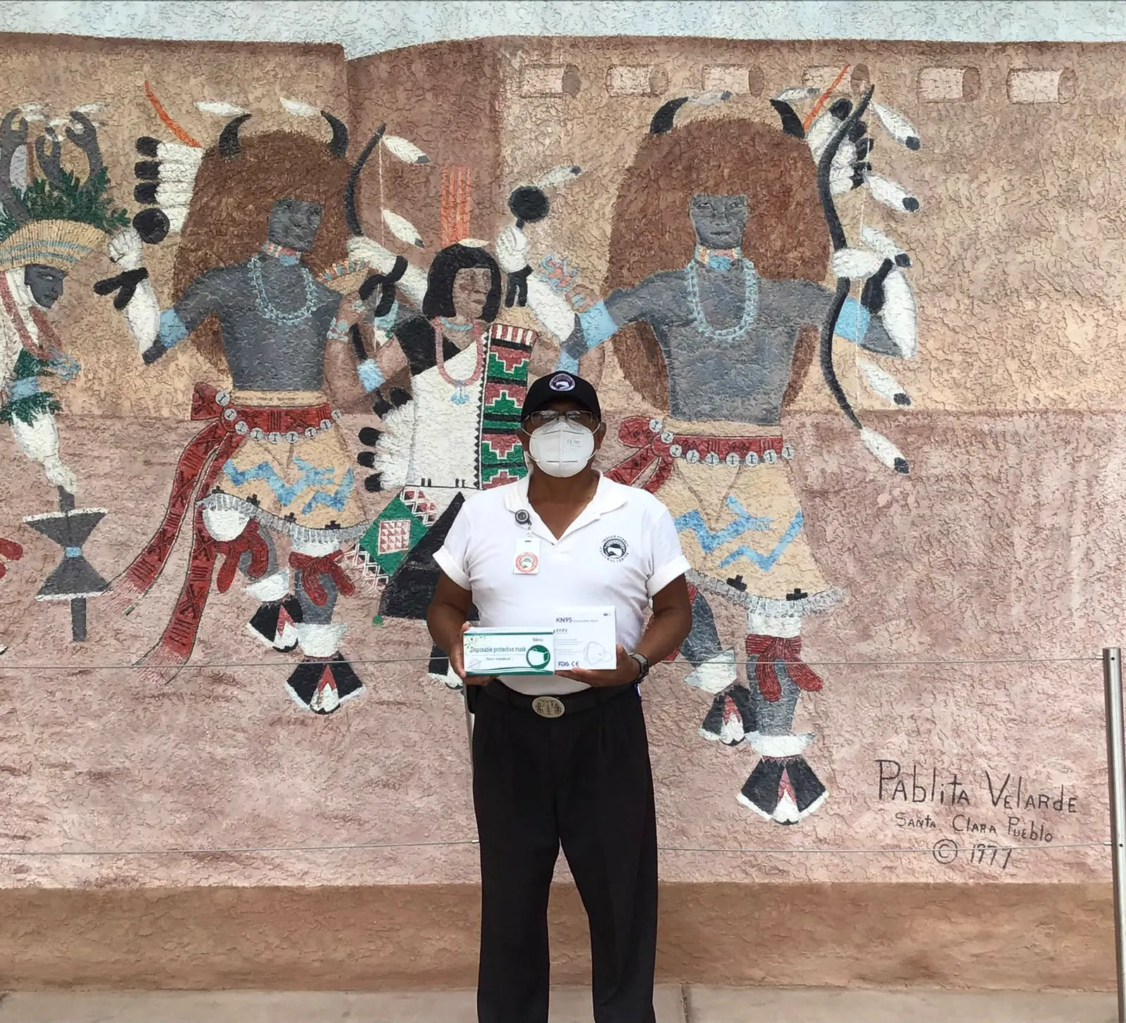 A man holding boxes of protective masks in front of a painted mural of dancers