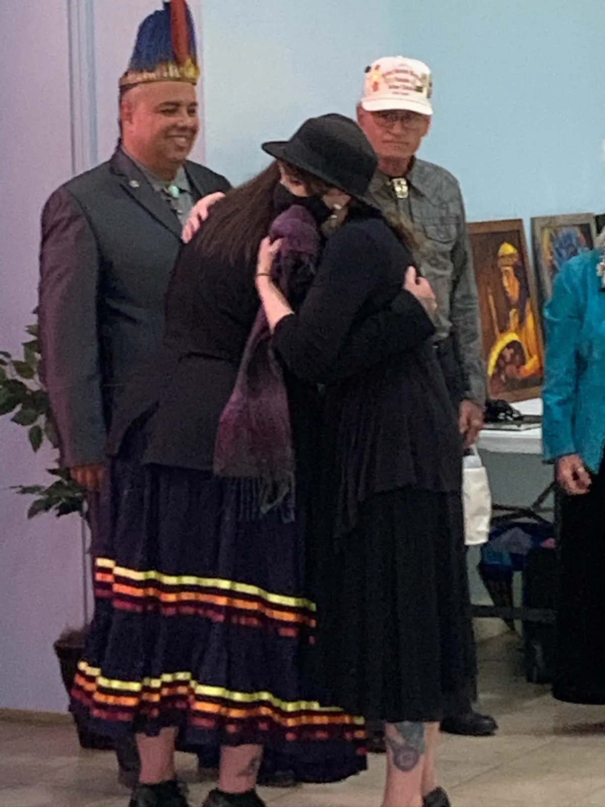 Two people embracing while others stand nearby at an indoor gathering