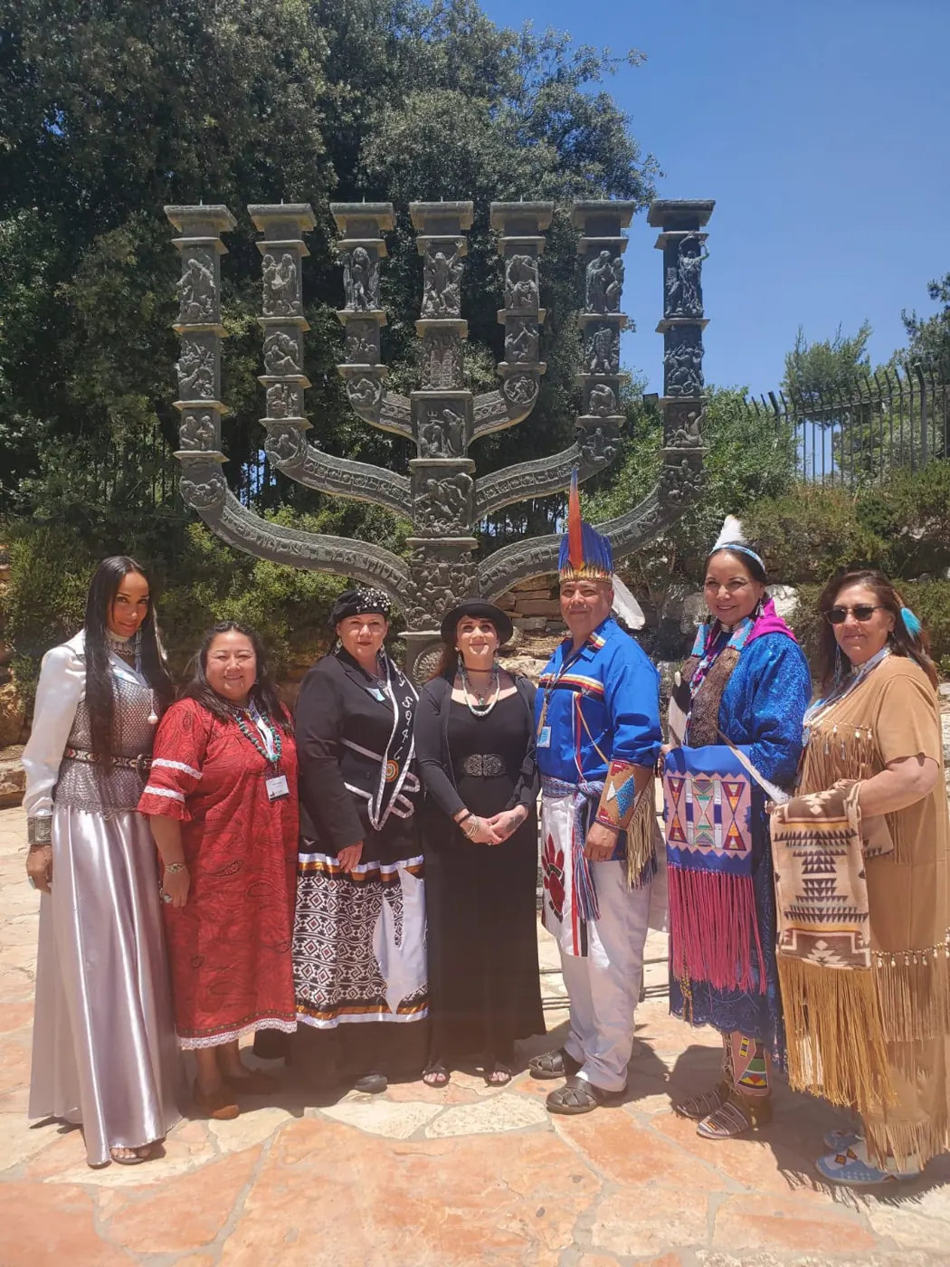 Seven people in colorful clothing standing outdoors before a carved monument