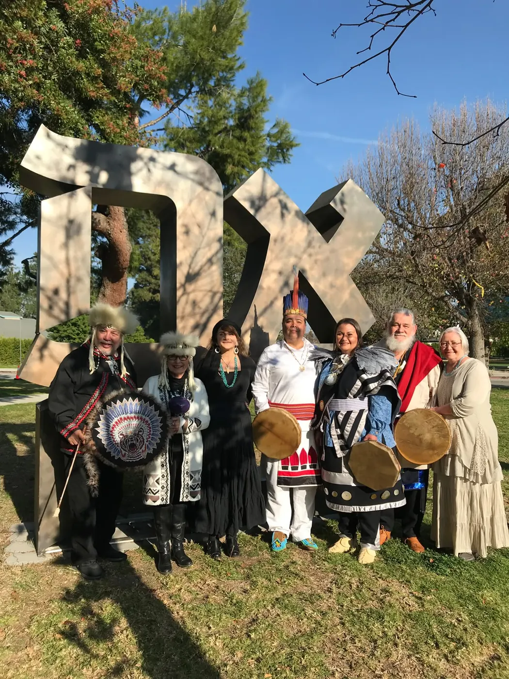 A group of people with drums standing outdoors before a large sculpture