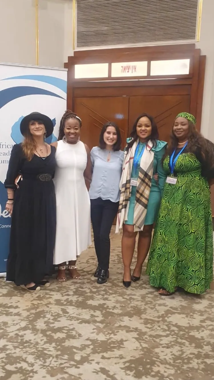 Five women standing together in front of wooden doors at a conference venue