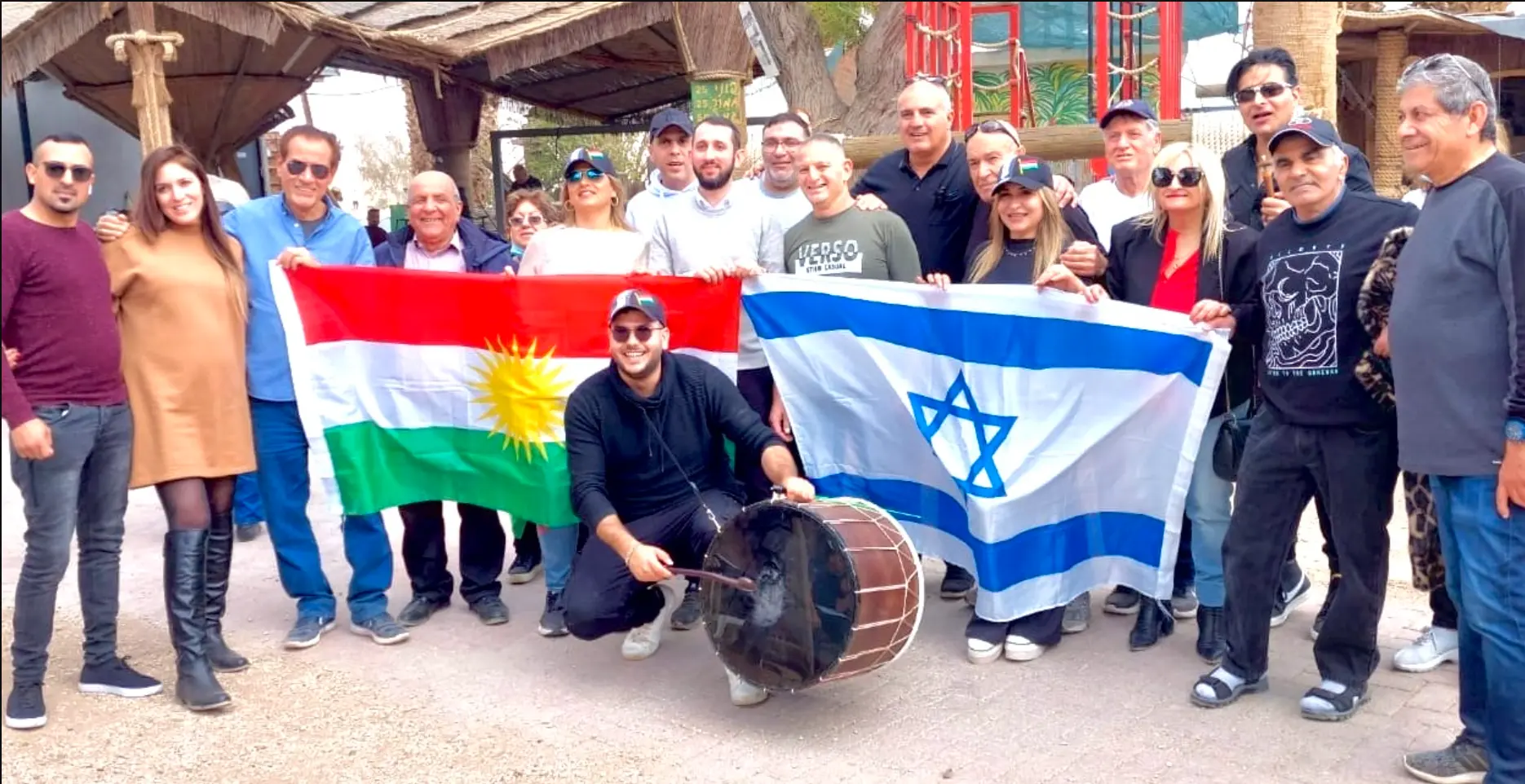 Kurdish and Jewish community members gathered outdoors holding Kurdish and Israeli flags.