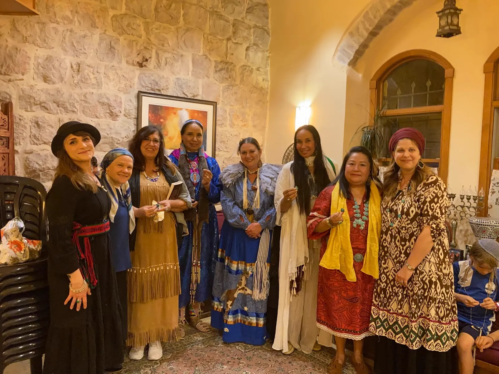 A group of women in traditional and contemporary dress standing together in a stone-walled room