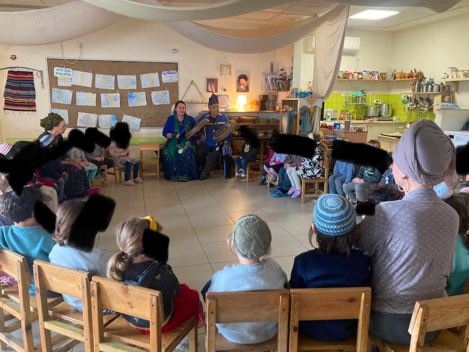 Adults and children seated in a circle around two people playing drums