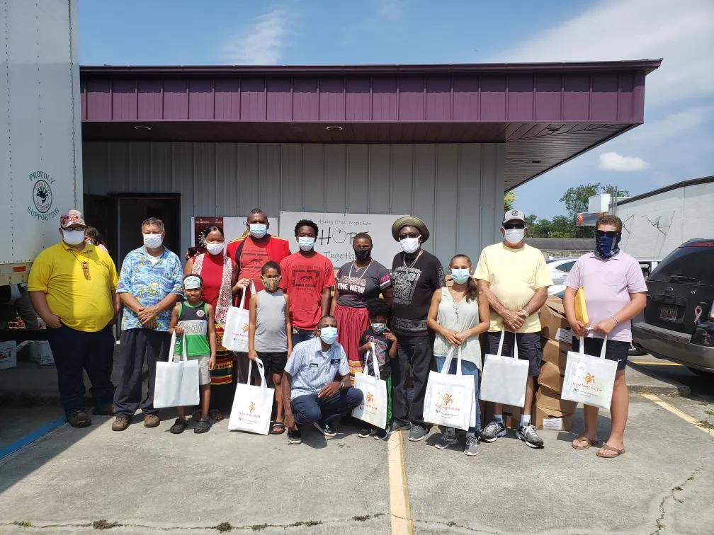 A large group outdoors holding gift bags in front of a community building
