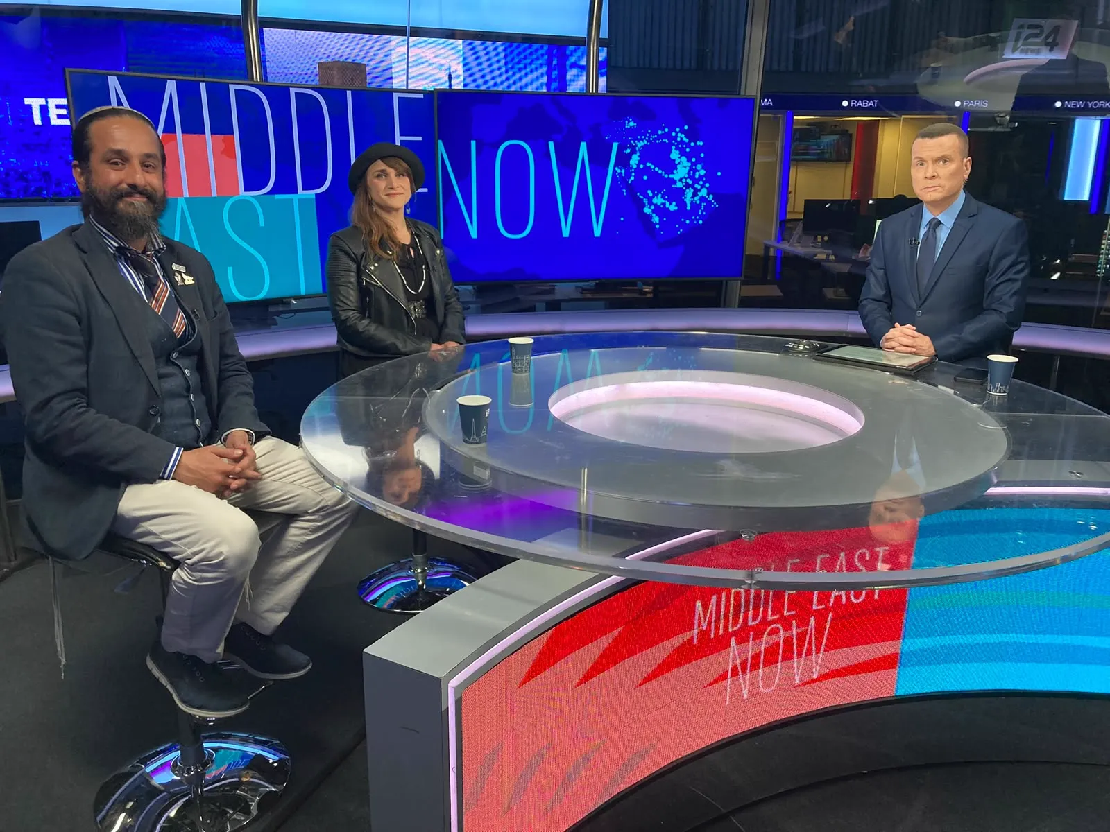 Three people seated at a curved glass desk in a television news studio
